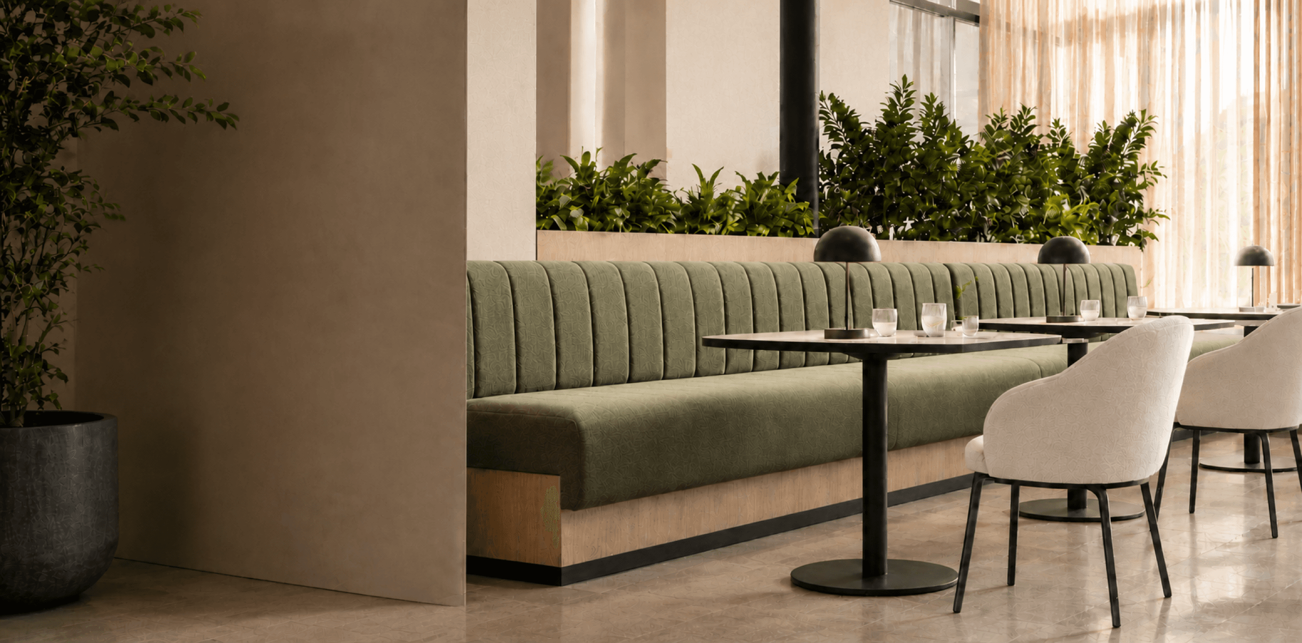 Warm, plant-filled restaurant interior with upholstered booth seating